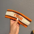 Detail of knitted sports headband with orange GRVR letters and checkered pattern - Beige + Orange