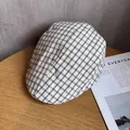 Detailed view of a black and white plaid flat cap on a wooden table with magazines - M / White