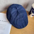 Top view of a dark blue denim beret hat on a wooden desk with decorative accessories - M / Navy Blue