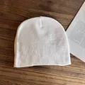 Berretto in maglia bianca su superficie di legno accanto a un libro per stile invernale - M / Bianco