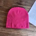 Dettaglio in piano di un berretto in maglia rosa acceso su superficie di legno e carta - M / Rosa Rosso