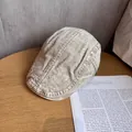 Dettaglio della trama del berretto piatto beige in lino lavato su un tavolo di legno - M / Beige