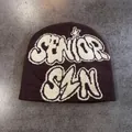 Macro detail of the dark brown knitted beanie featuring white jacquard graffiti lettering - M / Coffee