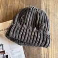 Detalle del gorro de punto gris oscuro con elementos desgastados sobre fondo de madera - M / Gris