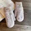Detail of warm plush mittens in beige with knitted cuffs and deer leather patch on wood - One Size / Khaki