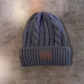 Detail van een donkergrijze kabelgebreide muts met een vintage lederen logo-patch erop - Grijs
