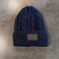 Detail van de marineblauwe kabelgebreide muts met een bruine leren patch met reliëf - Marineblauw