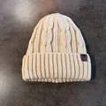 Dettaglio del cappello in maglia a trecce beige con toppa in pelle di alta qualità - Elastico / Beige