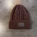 Detail van de kabelgebreide textuur van een donkerbruine wintermuts met een leren patch - koffiekleur
