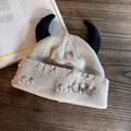 Macro detail of beige knit beanie featuring black ox horns, metal rings, and safety pin - Beige