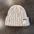 Dettaglio del berretto in maglia crema con riflessi blu e toppa in tessuto cucita - Beige / Elastico