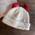Dettaglio del berretto bianco usurato con corna da diavolo rosse, spilla e anelli d'argento - Bianco Con Corna Rosse