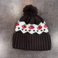 Dettaglio del berretto in maglia con motivo jacquard fragola e pompon in pelliccia nera - caffè