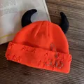 Detail of orange distressed beanie with black devil horns and silver metal safety pins - Orange