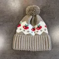Dettaglio ravvicinato del cappello in maglia con motivi a onde bianche e decori a ciliegia - Cachi