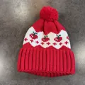 Dettaglio del berretto in maglia rossa con motivo jacquard a ciliegia e pompon morbido - Rosso
