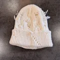Nahaufnahme der cremefarbenen Strickmütze mit Löchern und ausgefransten Quastendetails - M (54-59cm) / Weiß