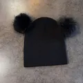 Dettaglio del berretto in maglia nera con due grandi pompon in finta pelliccia su sfondo - M / Nero