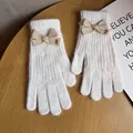 Dettaglio dei guanti in maglia color crema con fiocco kaki ed etichetta Baby decorata - Bianco