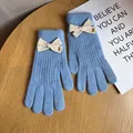 Close-up of sky blue knitted gloves with cream bow decoration and Baby label detail - Blue