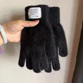 Detailansicht schwarzer Plüsch-Handschuhe mit dekorativem weißen Textaufnäher am Handgelenk - Schwarz