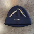 Detailopname van een donkerblauwe gebreide muts met witte golfpatronen en borduursels - M (55-59cm) / Marineblauw