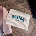 Detail von cremeweißem Strick-Stirnband mit grünem Boston-Schriftzug auf einem Holztisch - Gebrochenes Weiß