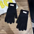 Nahaufnahme schwarzer Strickhandschuhe mit weißem Webeetikett auf Holzgrundlage - Einheitsgröße / Schwarz