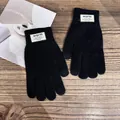 Detail of black winter knit gloves showing twill texture and warm label on wood surface - One Size / Black