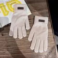 Detail van beige gebreide handschoenen met bruin label op een houten tafel achtergrond - Eén maat / Beige