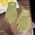 Detailaufnahme grüner Strickhandschuhe mit Webetikett auf einem Holzgrund für den Winter - Einheitsgröße / Obstgrün