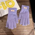Detailansicht lavendelfarbener Strickhandschuhe mit Lederlabel auf einem Holztisch - Einheitsgröße / Lila