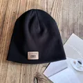 Detail of black knit beanie with a vintage brown leather patch on a wood surface - M / Black