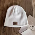 Detailed close-up of a white knit beanie featuring a brown leather logo patch on wood - M / White