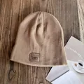 Detailed view of khaki knitted beanie featuring a premium leather brand label on wood background - M / Khaki