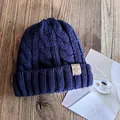 Close-up of navy blue cable knit beanie with premium square logo patch on wooden table - M (55-59cm) / Navy Blue