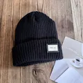 Close-up of black ribbed knit beanie featuring a CO. 1987 label on a rustic wooden surface - M (54-59cm) / Black