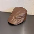 Detail shot of vintage dark brown PU leather beret showing fine texture and stitching - Camel