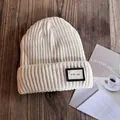Close-up of beige ribbed knit beanie with CO. 1987 patch on a wooden background - M (54-59cm) / Beige