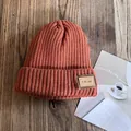 Detail of caramel knit beanie with vintage leather patch on a textured wood background - M (54-59cm) / Caramel color