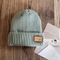 Close-up of sage green ribbed knit beanie featuring a vintage leather label on wood - M (54-59cm) / Teal