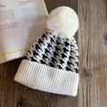 Close-up of houndstooth knit beanie with a fluffy faux fur pom-pom on wooden background - M / White