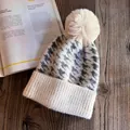 Detail of winter houndstooth knit beanie featuring a cream faux fur pom-pom on wood - M / Beige