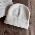 Gros plan d'un bonnet en maille côtelée blanche avec texture laineuse sur bois sombre - M / Blanc