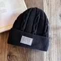 Detail of black cable knit beanie with fleece lining and City woven patch on wooden background - M (55-59cm) / Black