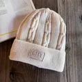 Detail of cream knit beanie featuring thick chain texture and leather brand label on a desk - M (55-59cm) / Beige