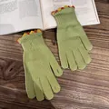 Detail von grünen Strickhandschuhen mit bunten Bommel-Bordüren auf einem Holzhintergrund - Grün