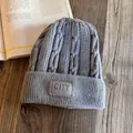 Detail of grey cable-knit beanie with a rectangular woven patch on a vintage wood desk - M (55-59cm) / Gray