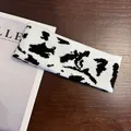 Knitted cow print headband for sports and casual wear placed on a wooden desk - Cow Print - Black