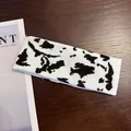 Detail view of the black and white cow print knitted sports headband on wood background - Cow Print - Coffee